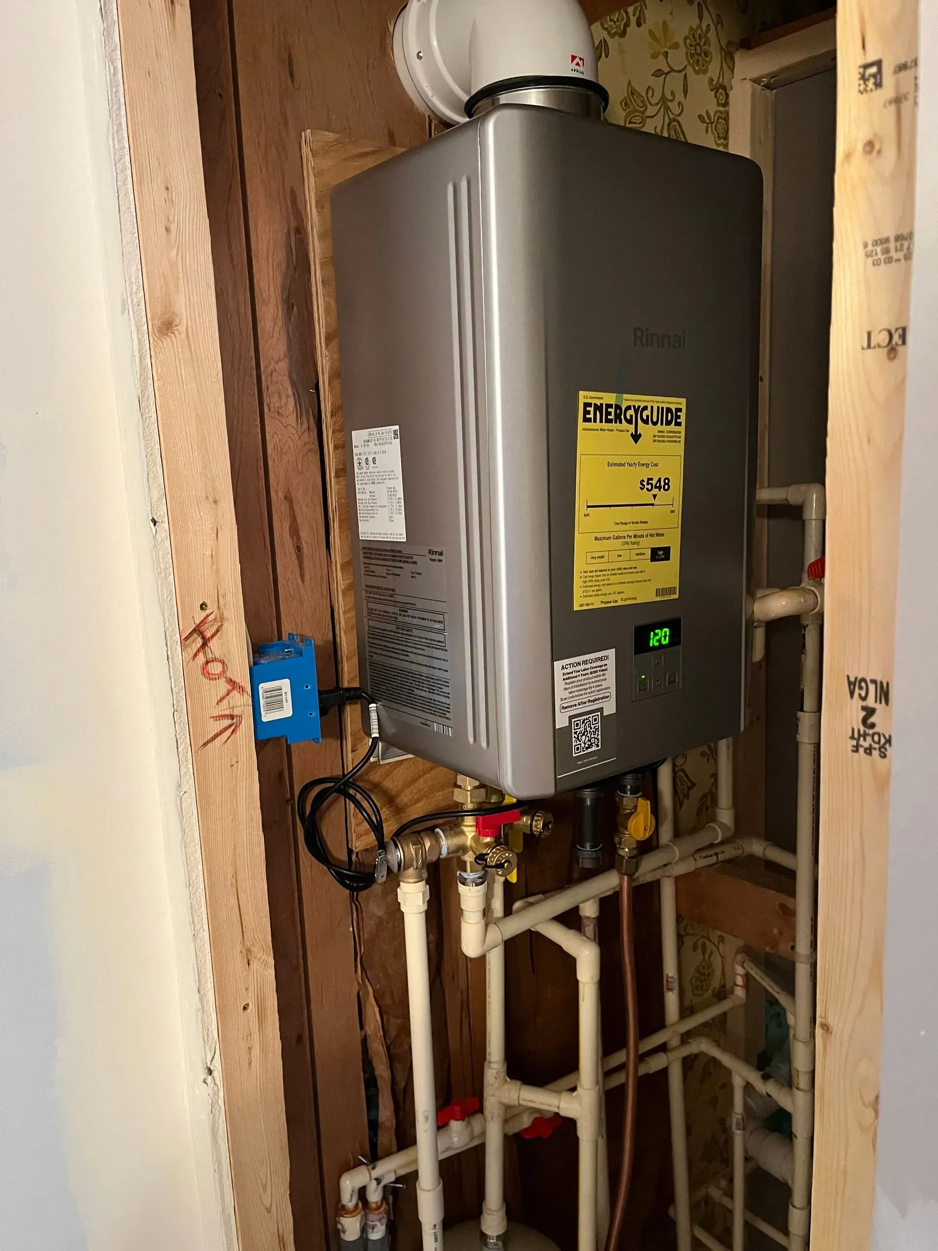 Wall-mounted gray tankless water heater with white pipes in a narrow utility closet