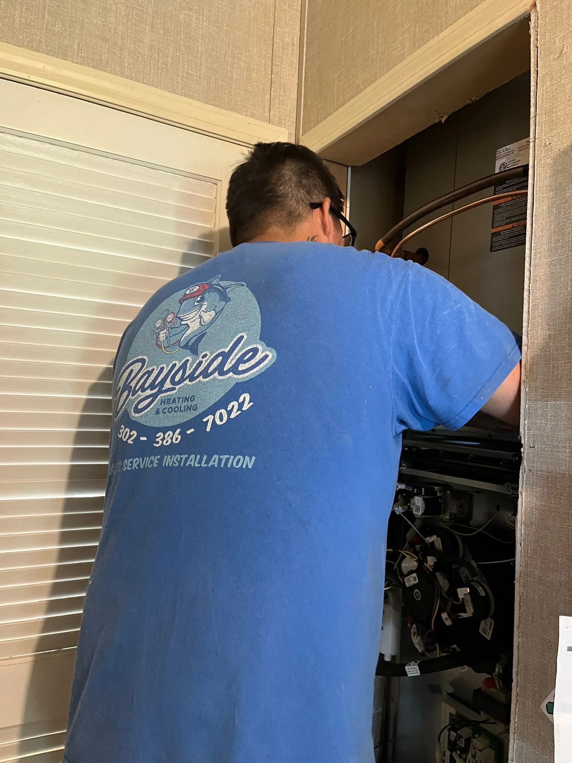 Technician in blue shirt working inside an open electrical panel cabinet.