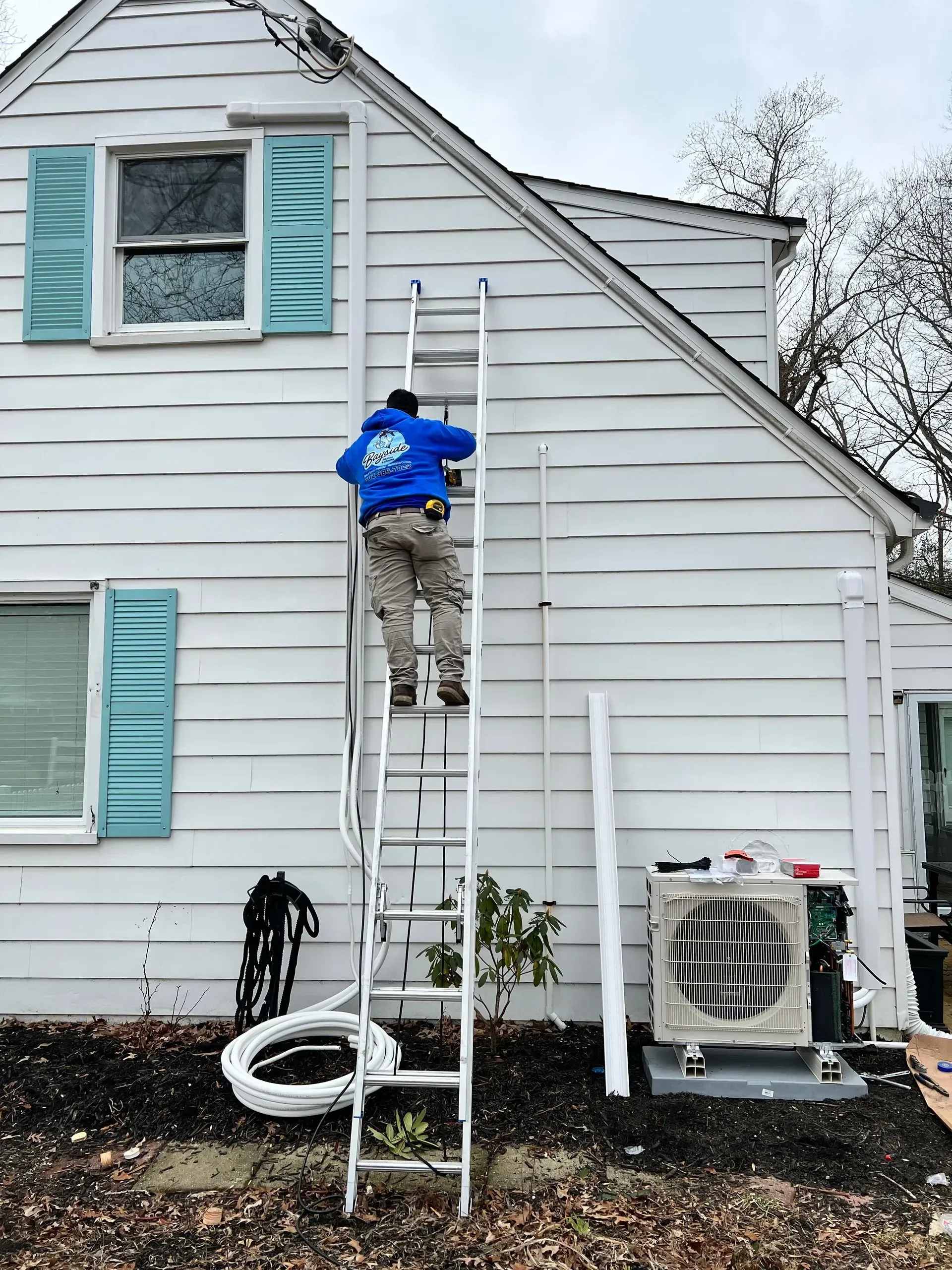 Person on a ladder painting a white house exterior with teal shutters