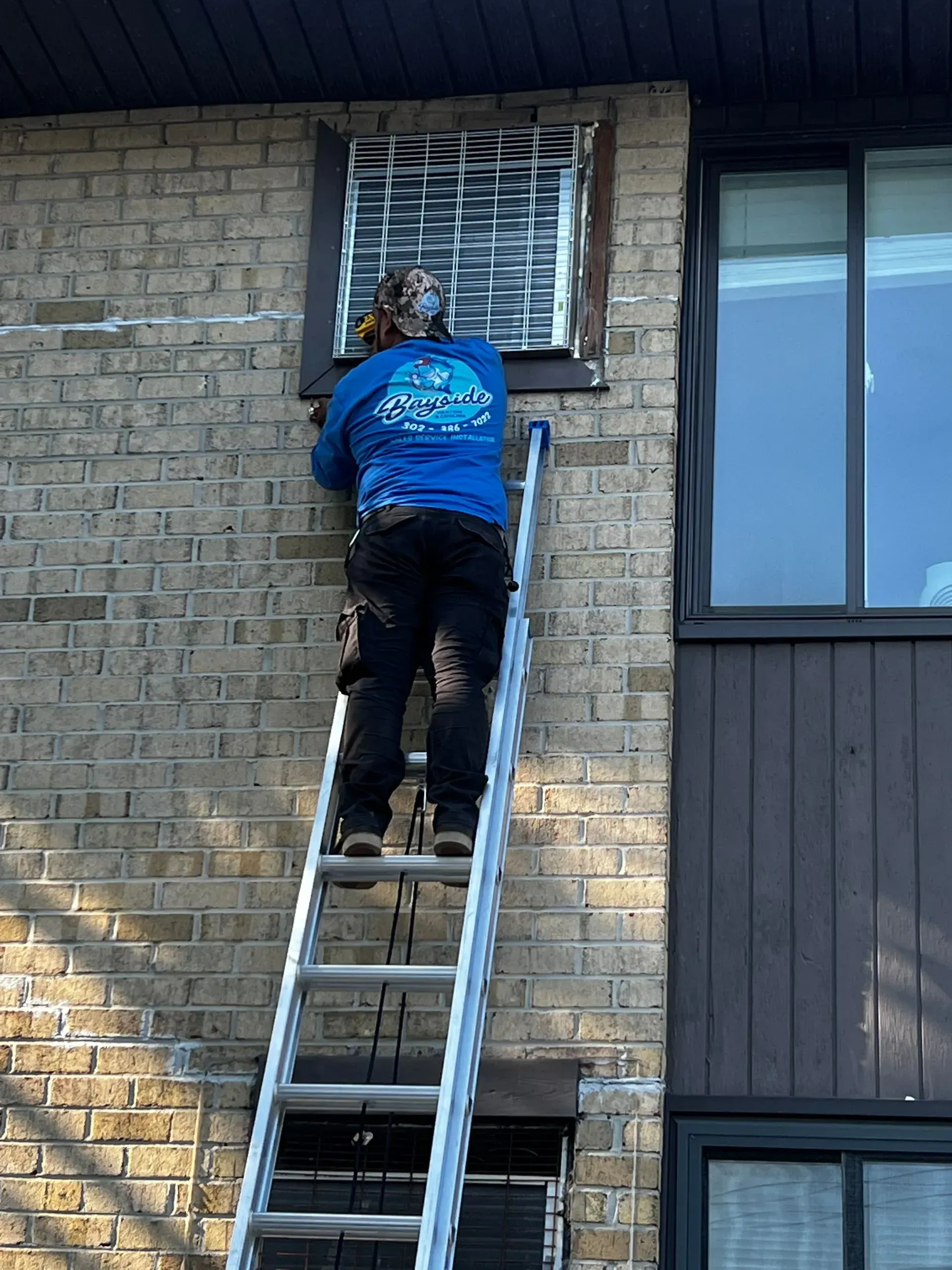 Person on a ladder working at a brick building window with metal bars