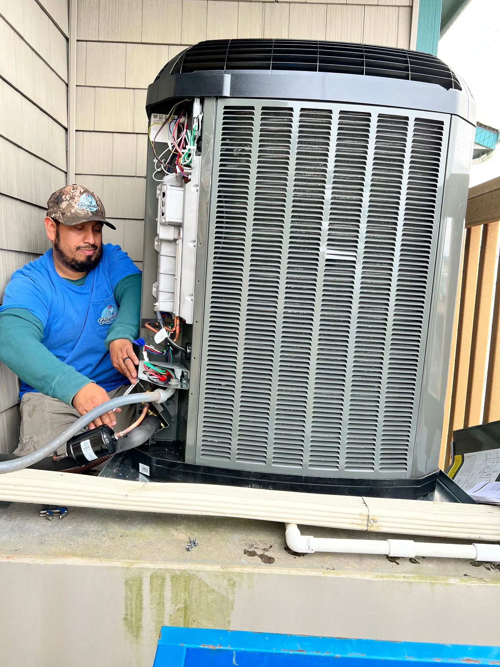 Technician servicing a large outdoor HVAC unit beside a house siding.