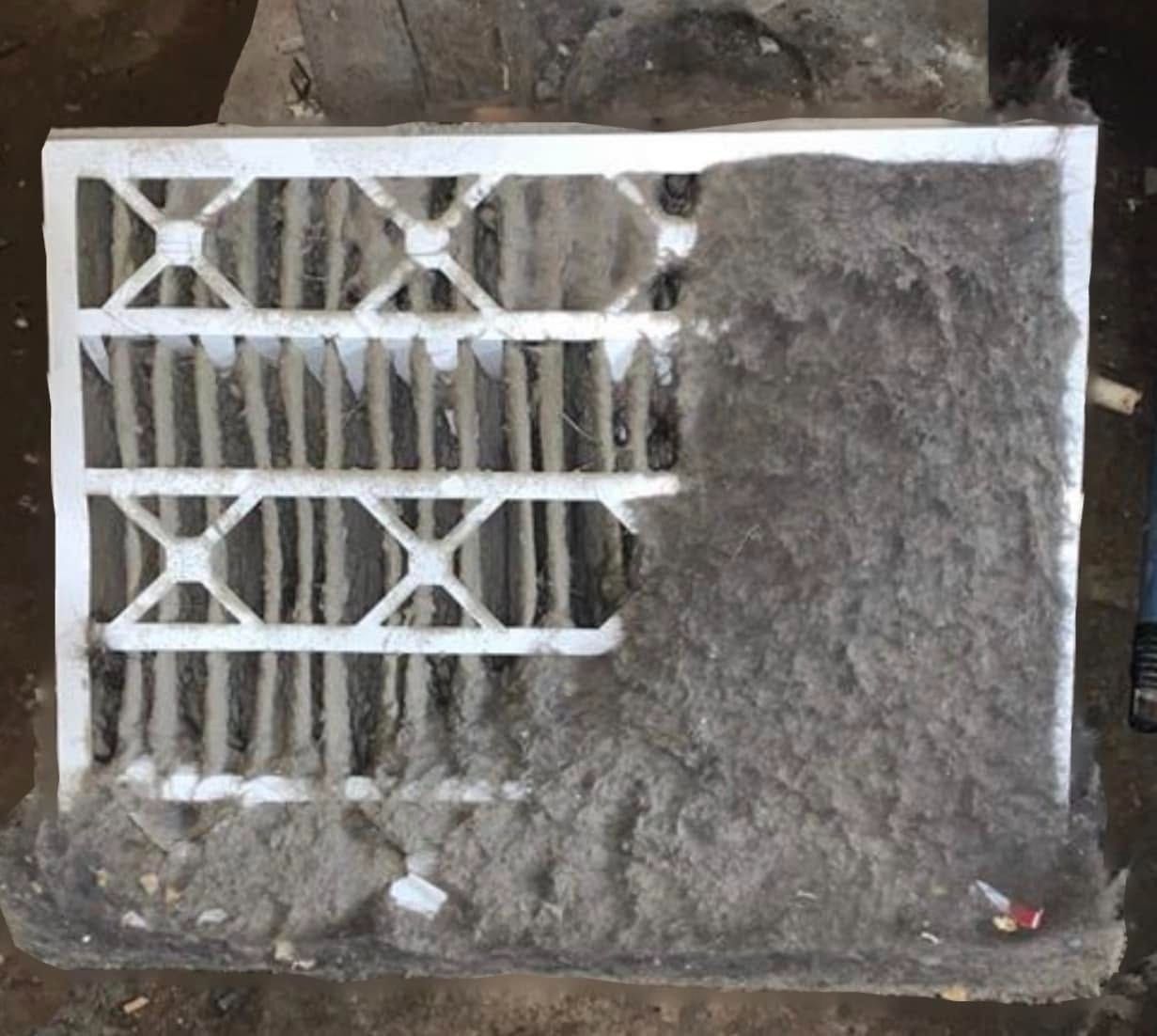 White metal vent grille partly buried in dirt and debris against a dark background