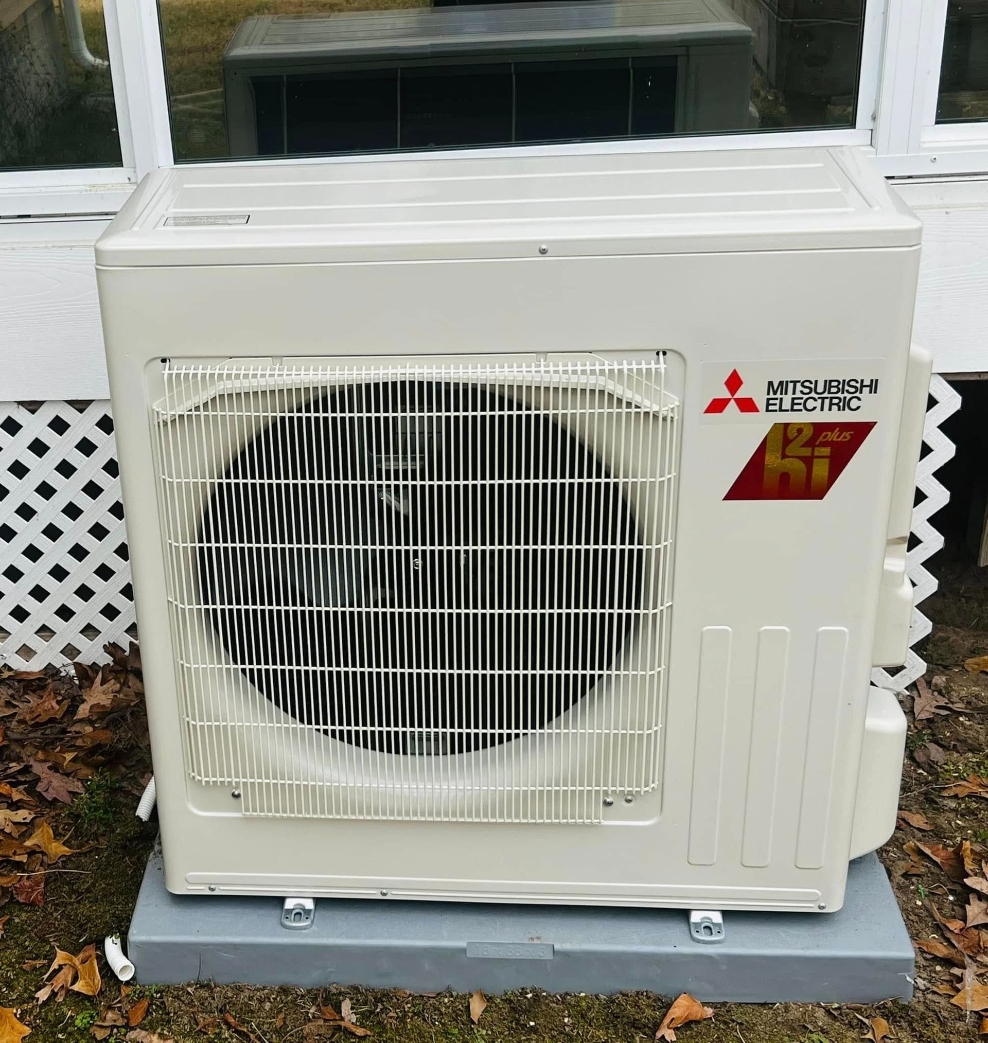 White Mitsubishi electric outdoor air conditioner unit on a concrete pad against a house wall.