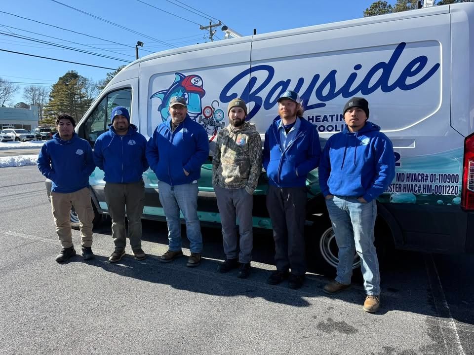 Six people in blue jackets stand beside a Bayside service van on a sunny street.
