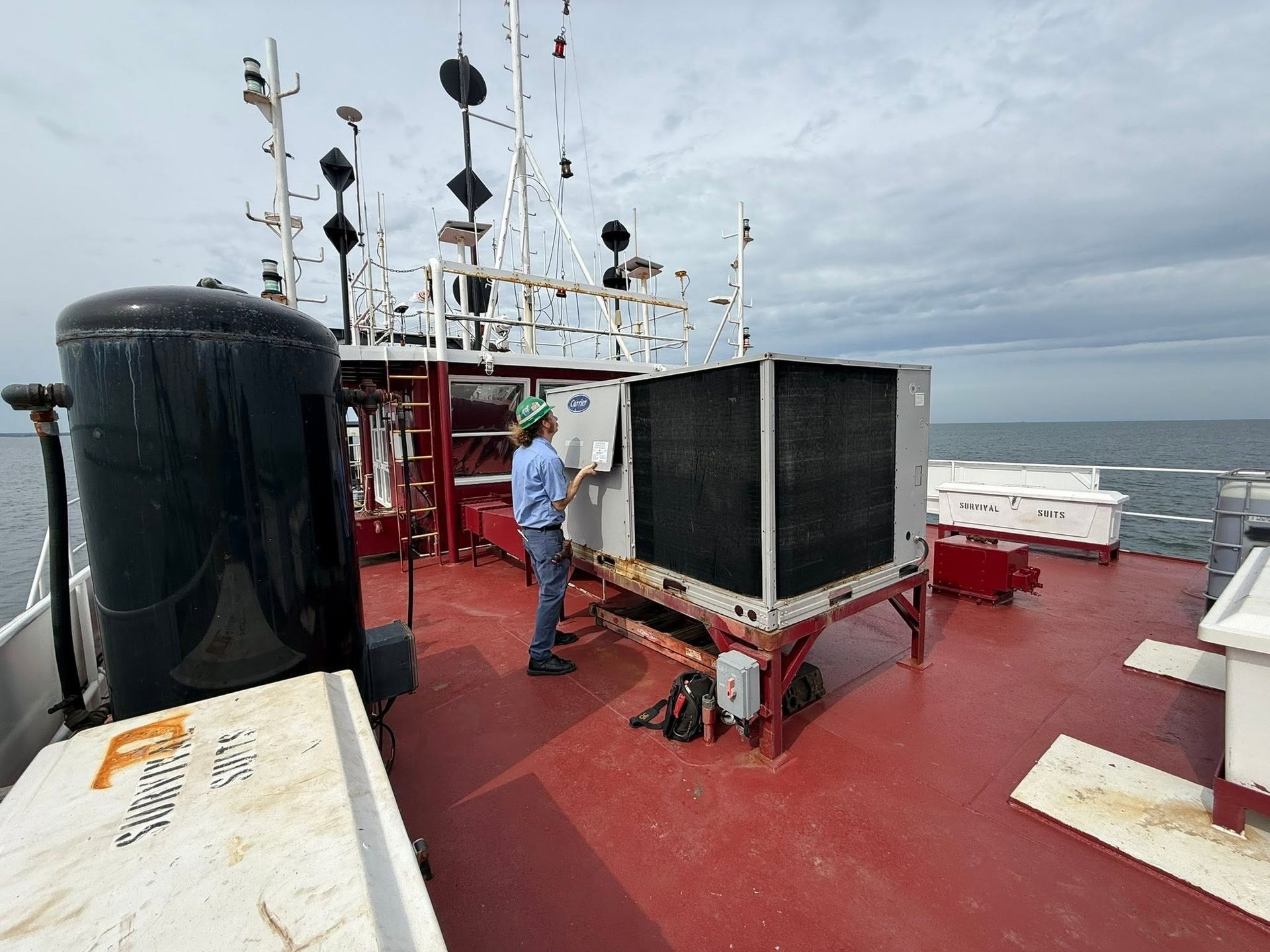 Crew member on a red ship deck beside black equipment and antennas under a cloudy sky