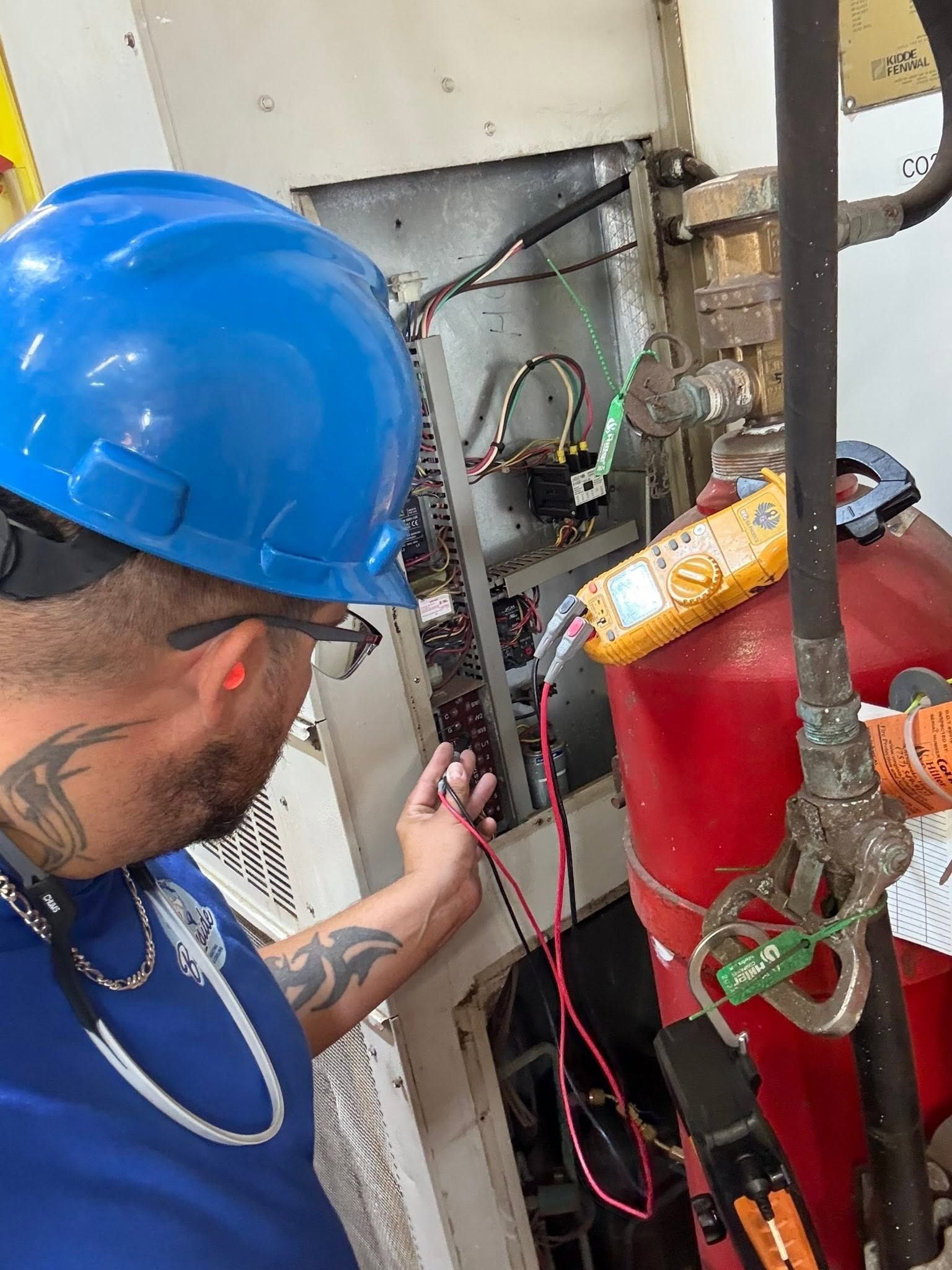 Worker in blue hard hat inspecting wiring beside red equipment in a utility area