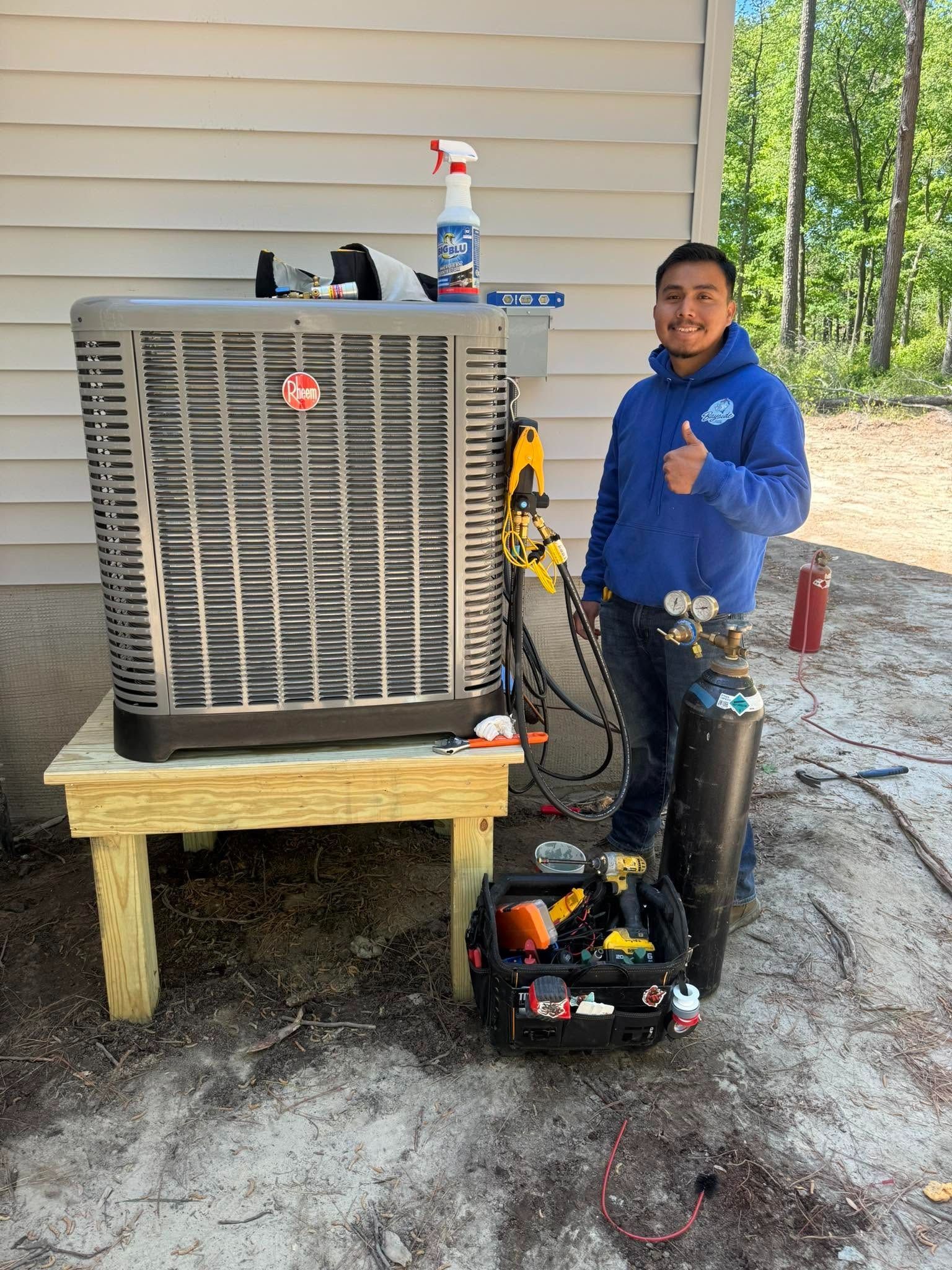 Technician beside HVAC unit outdoors, holding a thumbs-up and a tool cart with supplies.