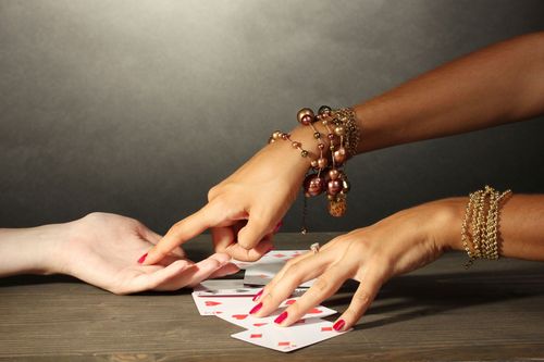 Hands reaching over playing cards on a table, suggesting a card reading or game.