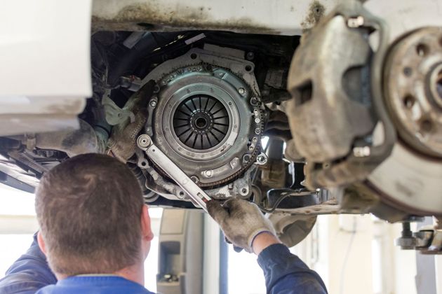 Mechanic inspecting a car’s exposed clutch assembly under the vehicle on a lift