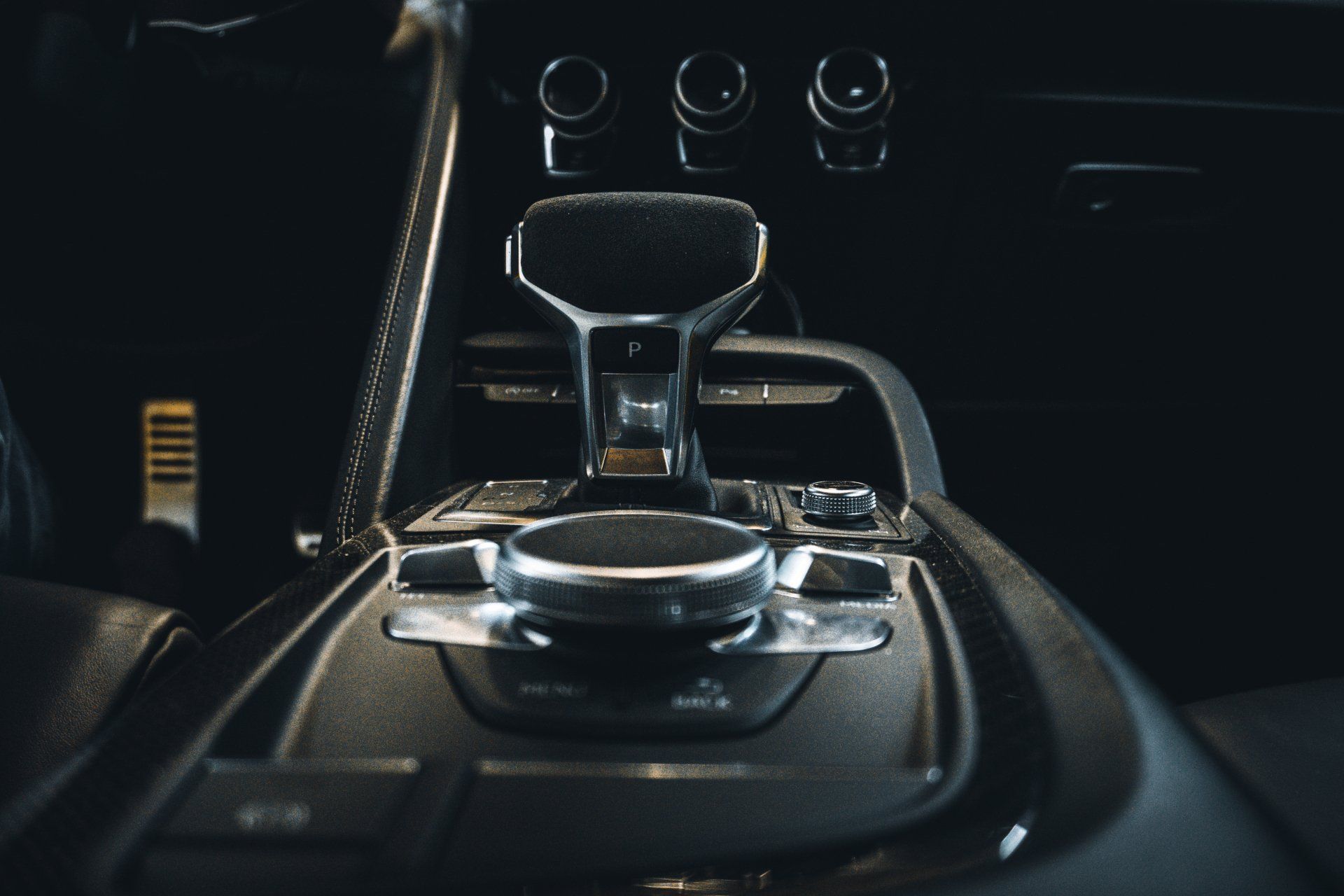 Luxury car center console with leather gear shifter and rotary control knobs in dark interior