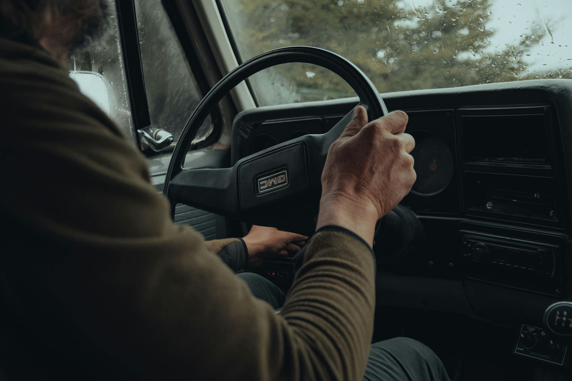 Driver’s hands on steering wheel inside a moving car, with a rainy road visible through the window