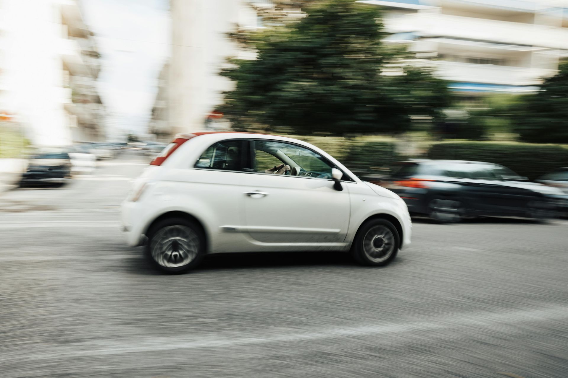 White compact car driving on a city street with motion blur in the background