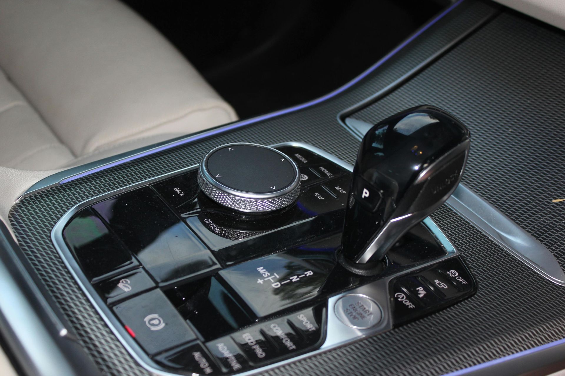 Car center console with glossy black gear selector and rotary control on a carbon-fiber trim panel