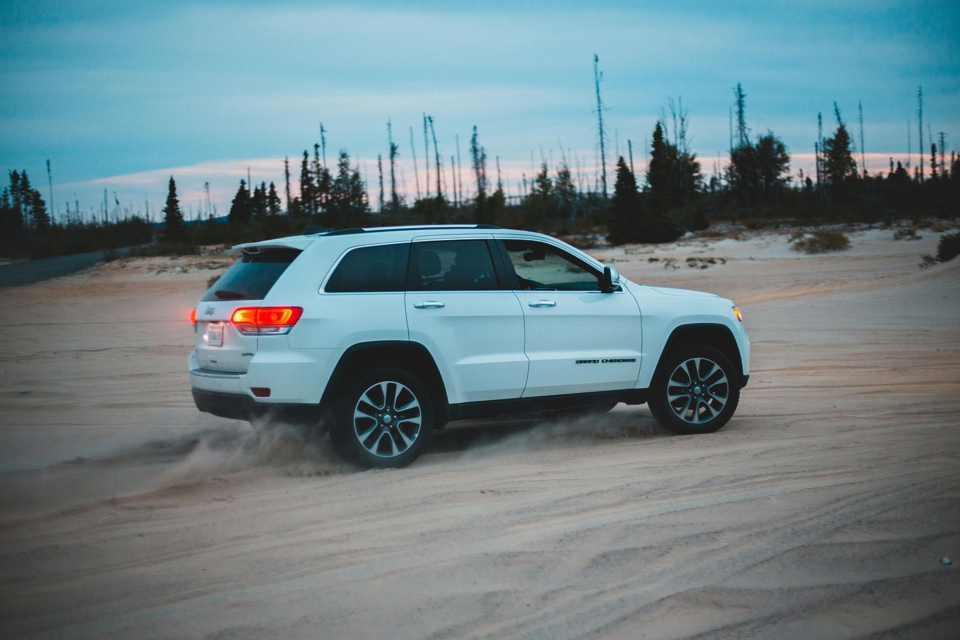 White SUV driving on a sandy dirt road at dusk with trees in the background