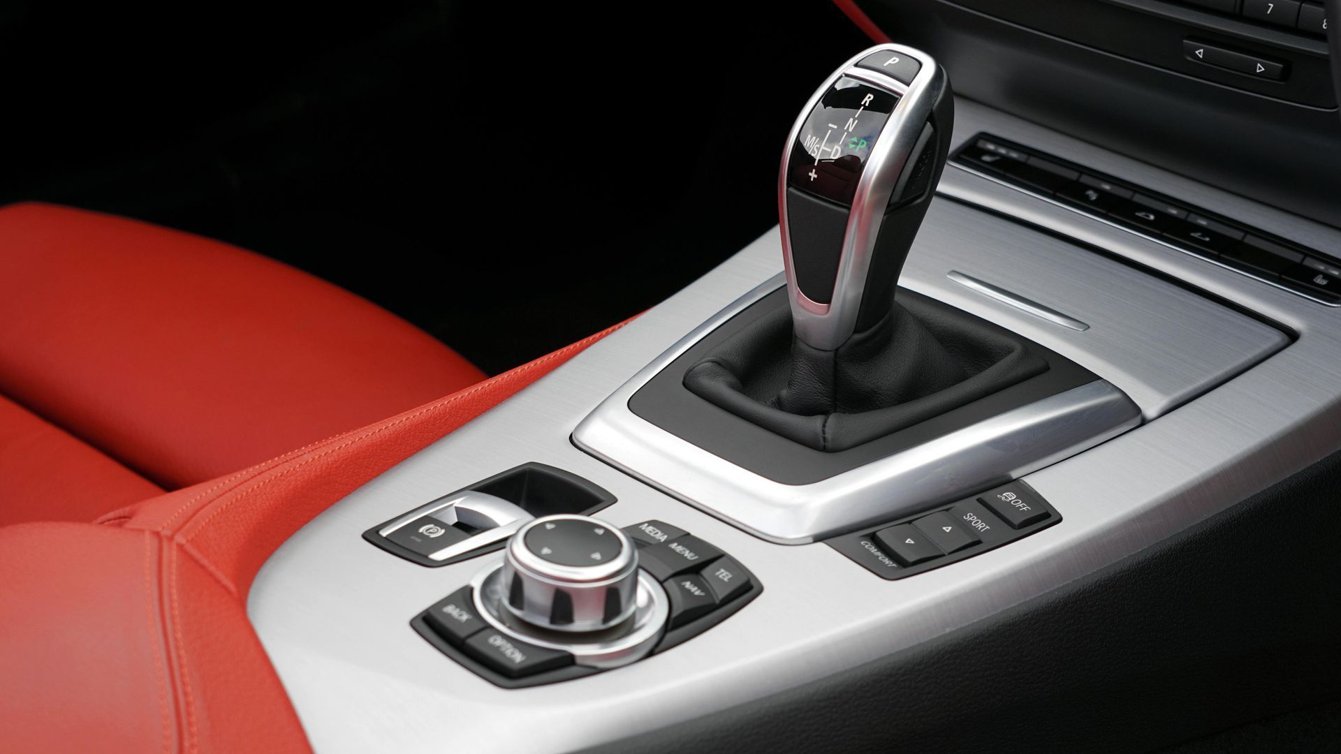 Car center console with automatic gear shifter and control dial, featuring red and silver trim