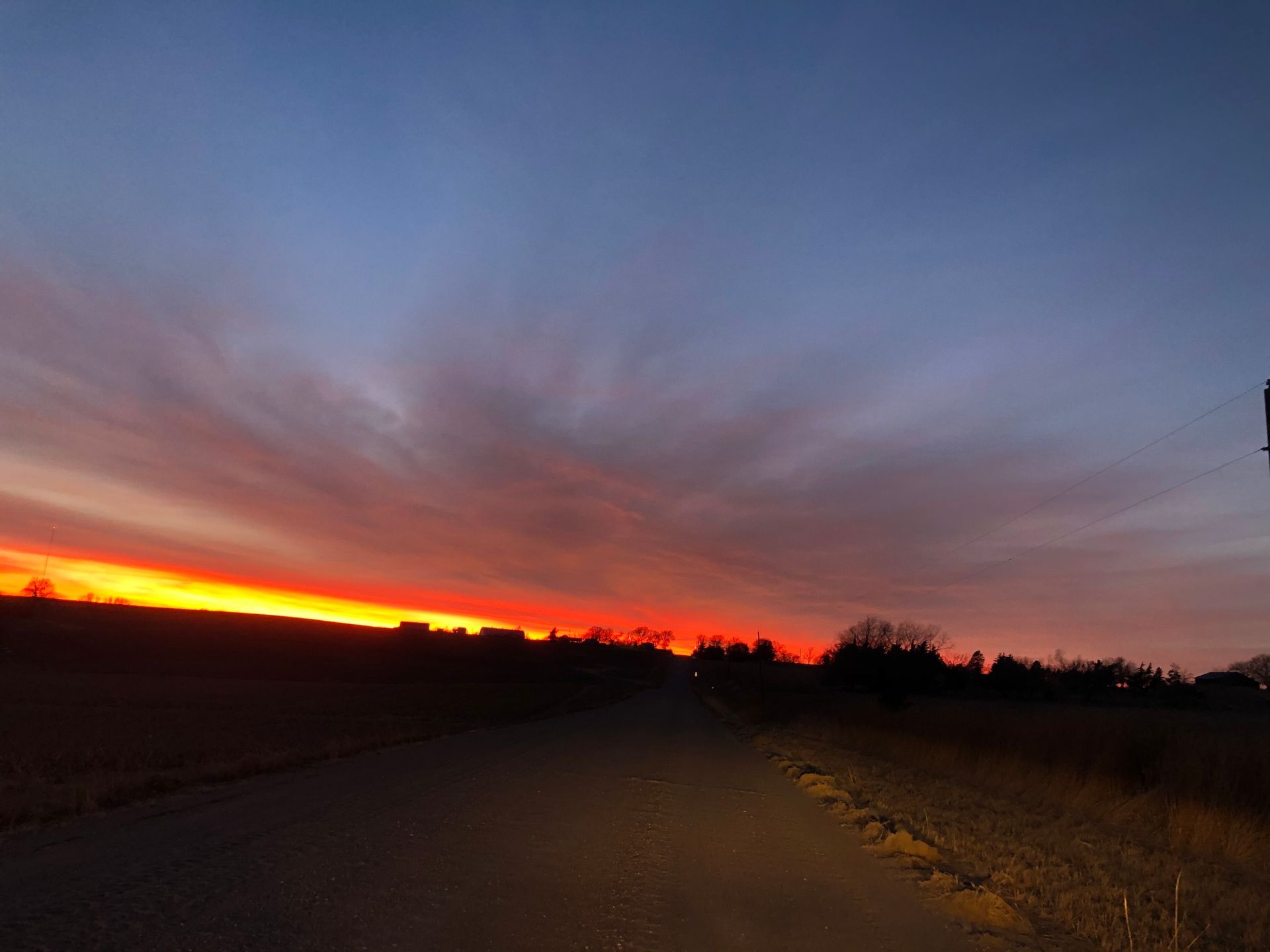 A sunset over a dirt road with a sign in the foreground.