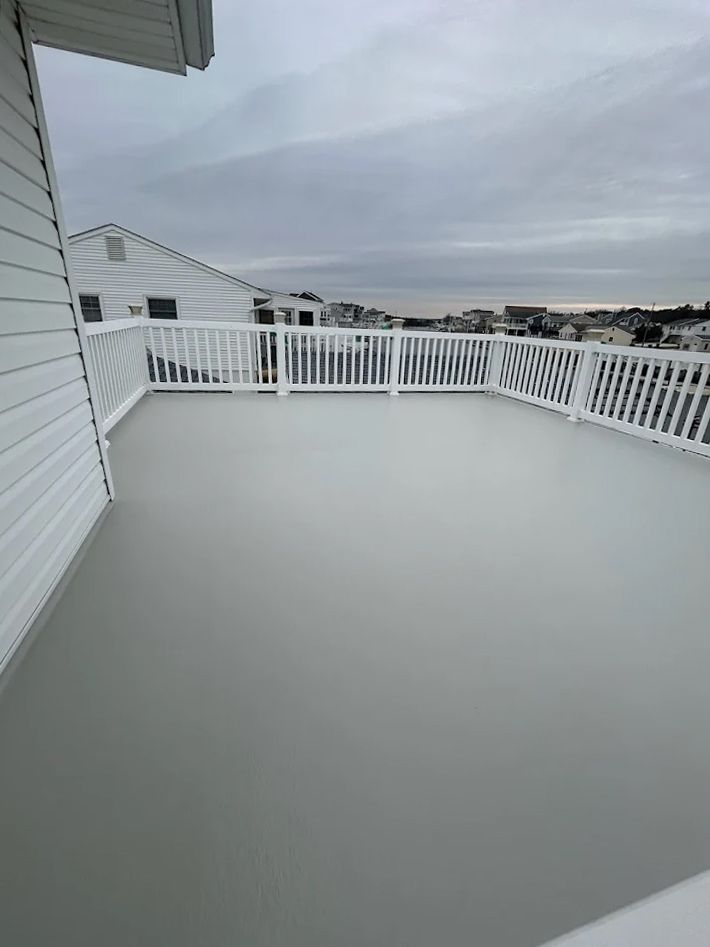 A large empty deck with a white railing and a view of the ocean.