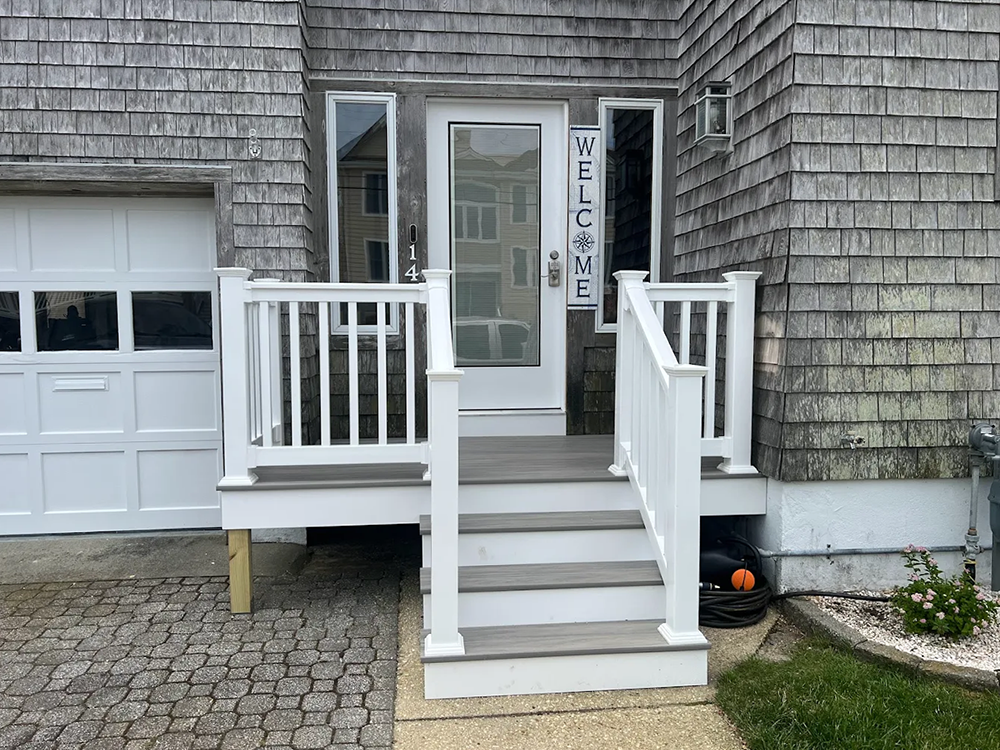 A white porch with stairs leading up to the front door of a house.