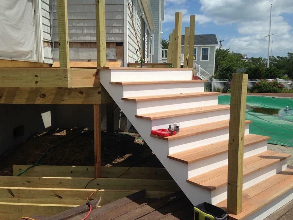 A wooden deck with stairs and a pool in the background