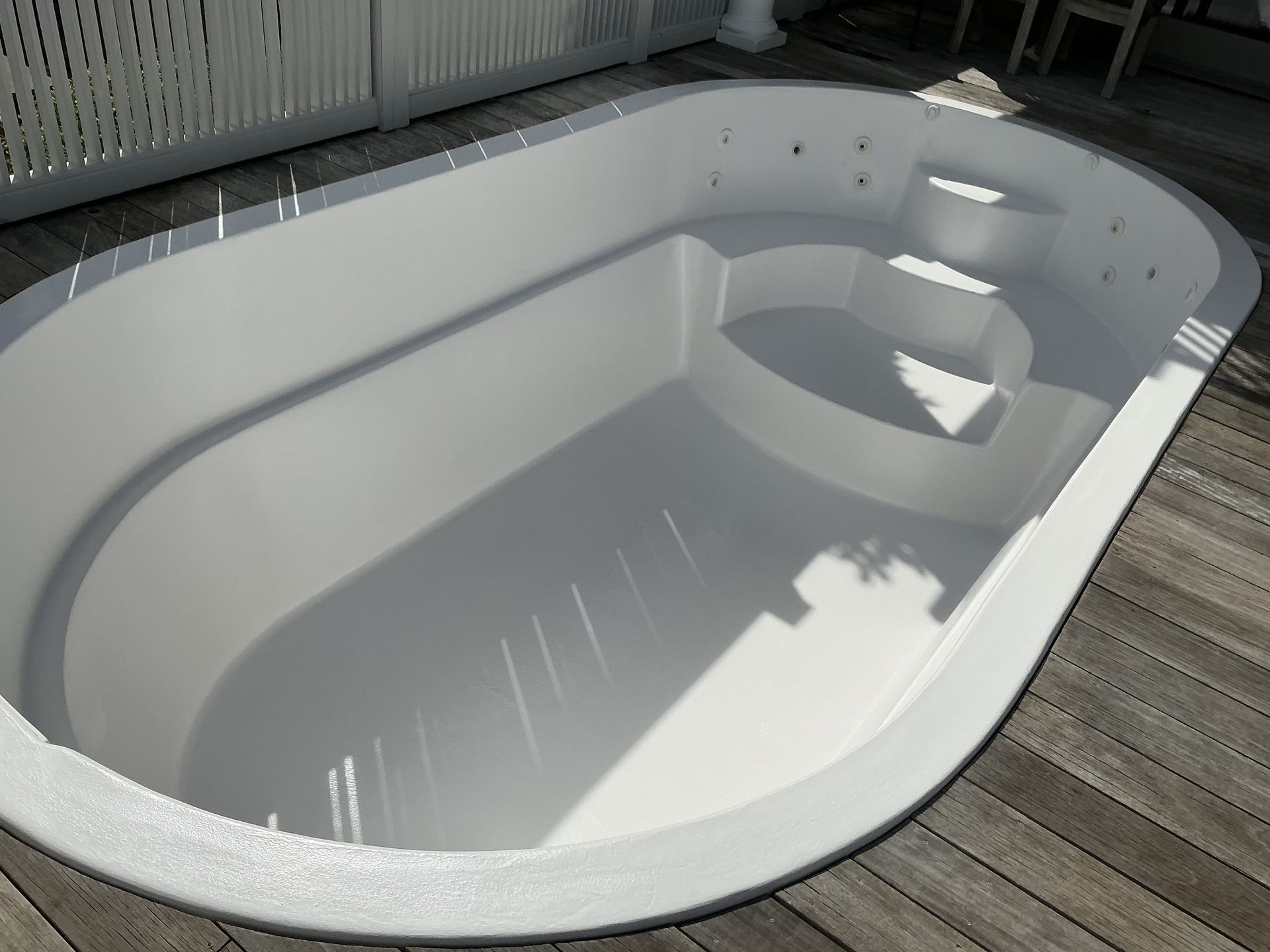 White, empty, oval-shaped hot tub with built-in steps, set on wooden deck.