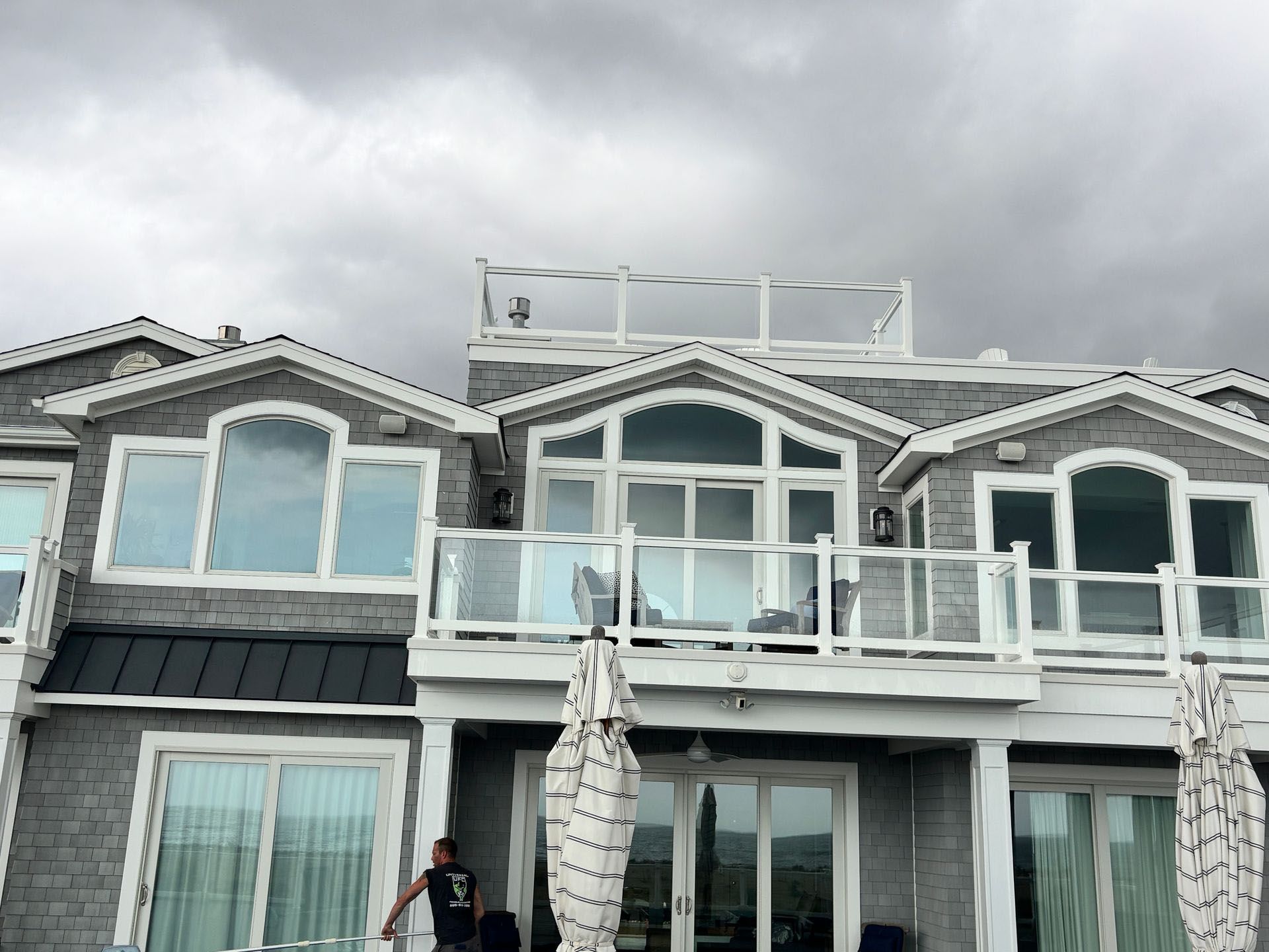 A man is standing in front of a large house with a balcony.