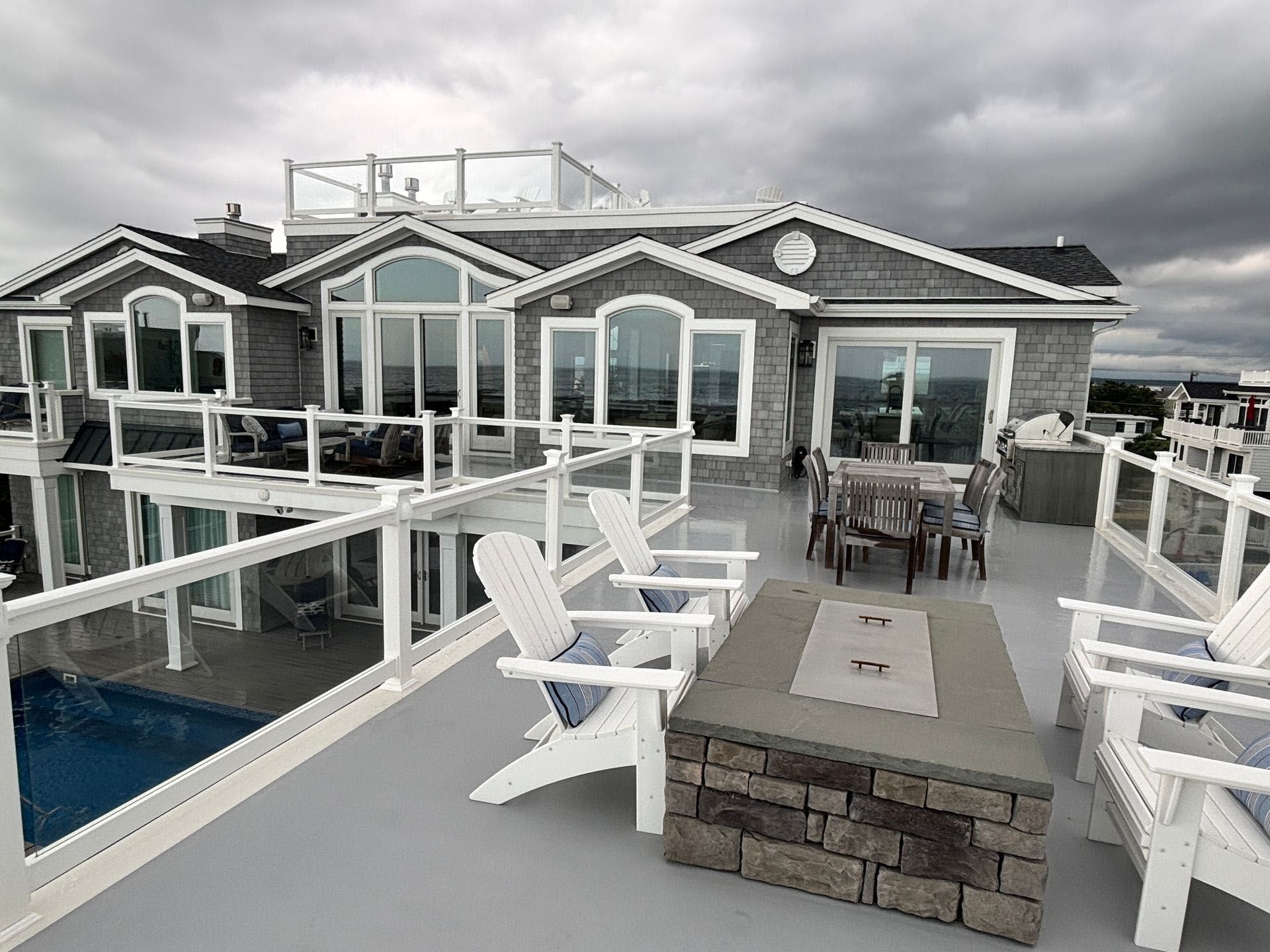 A large house with a large deck with chairs and a fire pit.