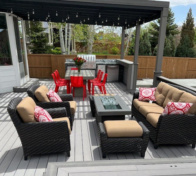 Patio with outdoor furniture, gray deck, pergola, red chairs, and grill.