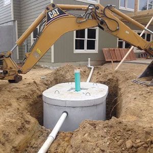 A cat excavator is digging a hole in the ground to install a septic tank.