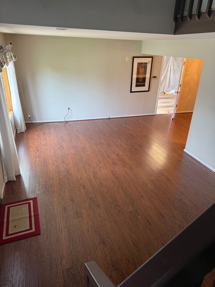 Empty living room with hardwood floors, light walls, artwork, and doorway.