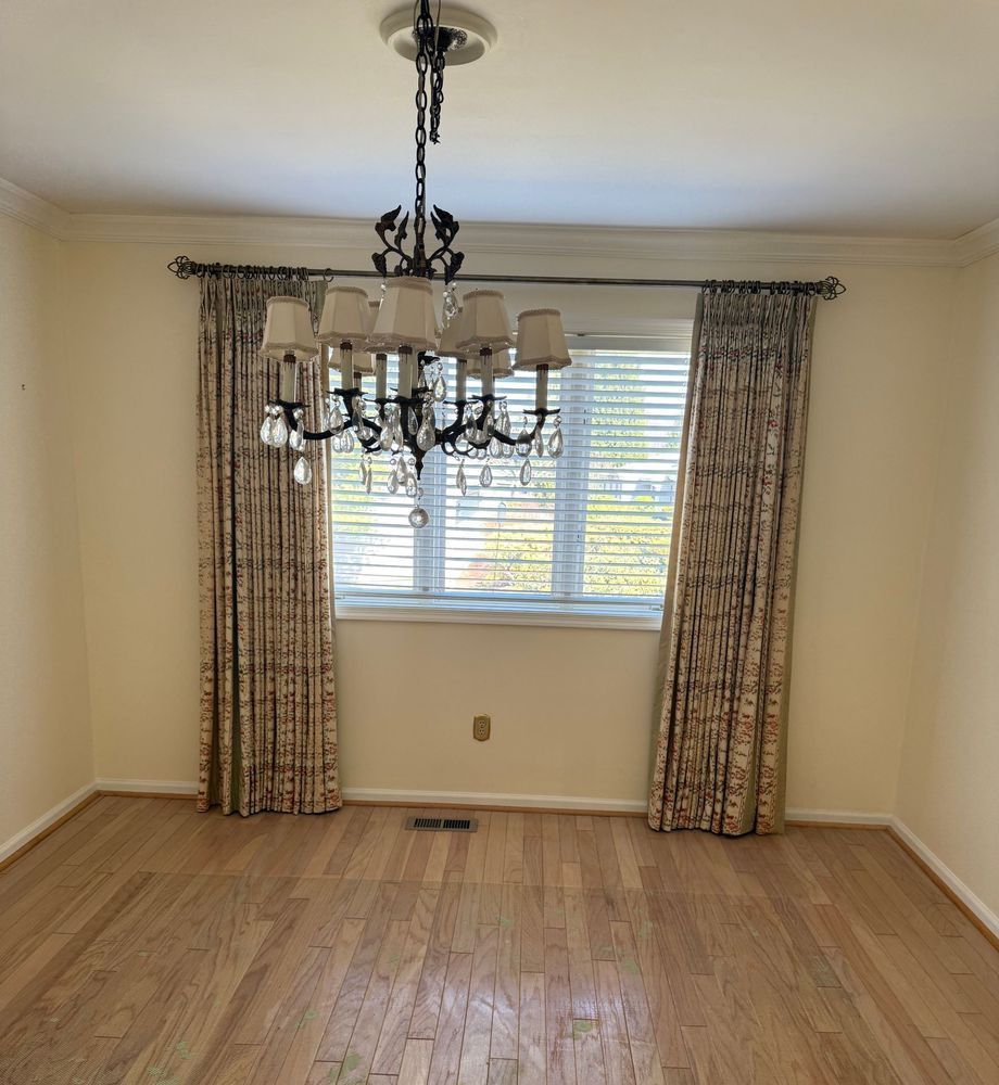 Empty room with a window, hardwood floor, chandelier, and patterned curtains.