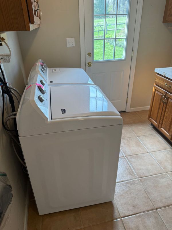 White washing machine and dryer in a laundry room, near a door and cabinets.