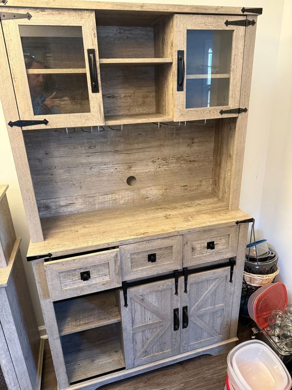 Light-wood, rustic-style hutch with glass-door upper cabinets, wine glass holders, and barn-door style lower cabinet.