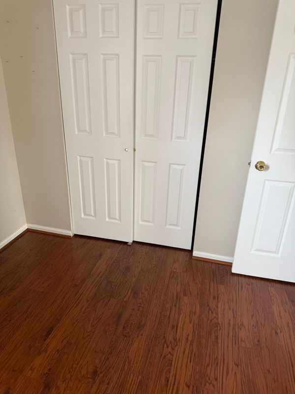 Room with wood-look flooring, white closet doors, and a partially visible door. Beige walls.