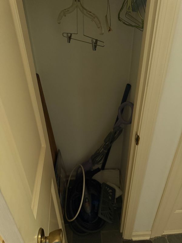 A cluttered closet with a broom, vacuum, and hangers; a doorknob is visible.