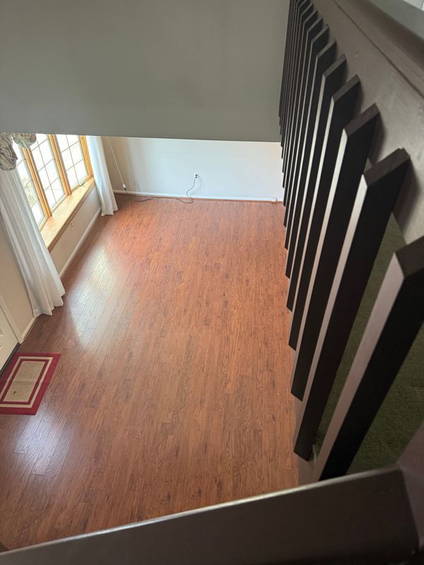 View from above of a room with wooden floors, staircase, windows with curtains and a red rug.