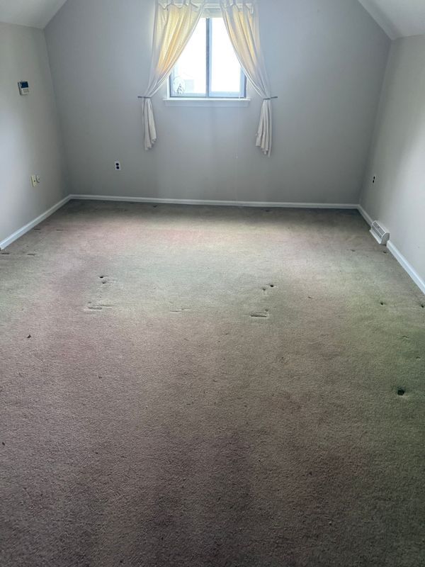 Empty room with sloping ceiling, small window with curtains, and brown carpet.