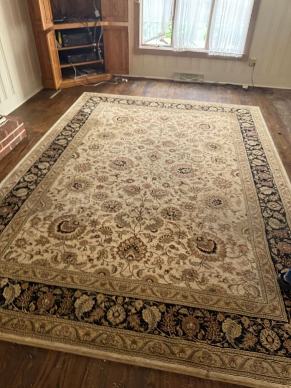 Large beige floral area rug on dark wood floor, with dark border.
