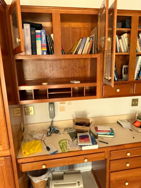 Wooden desk with cluttered surface, built-in shelving and cabinets, books, and open doors.