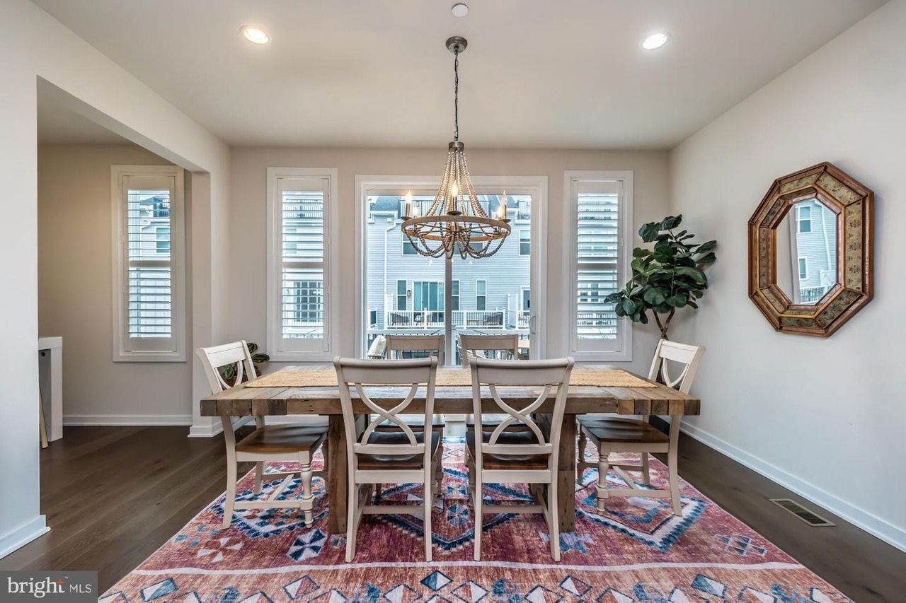 Dining room with wooden table, chairs, chandelier, and patterned rug.