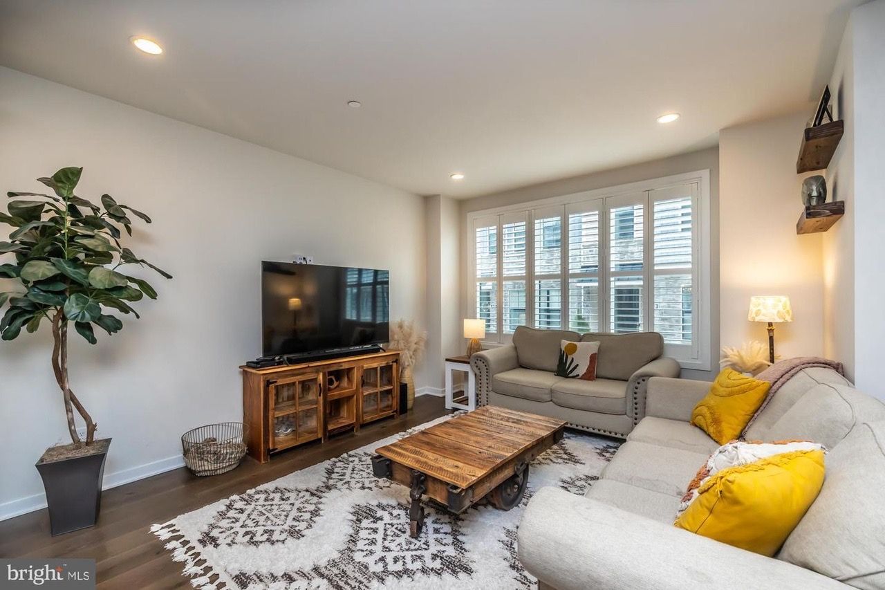 Cozy living room with sofa, TV, wooden coffee table, rug, and large window with shutters.