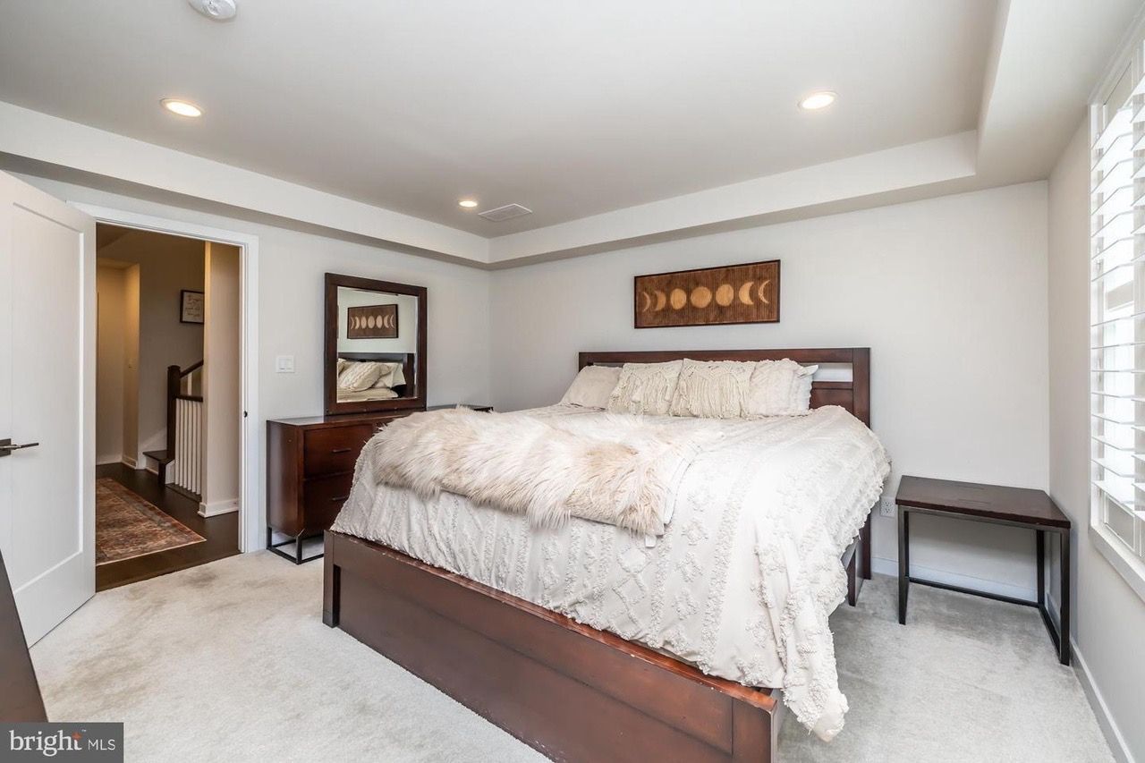 Bedroom with bed, nightstand, dresser, and doorway to hallway. White and brown color scheme.