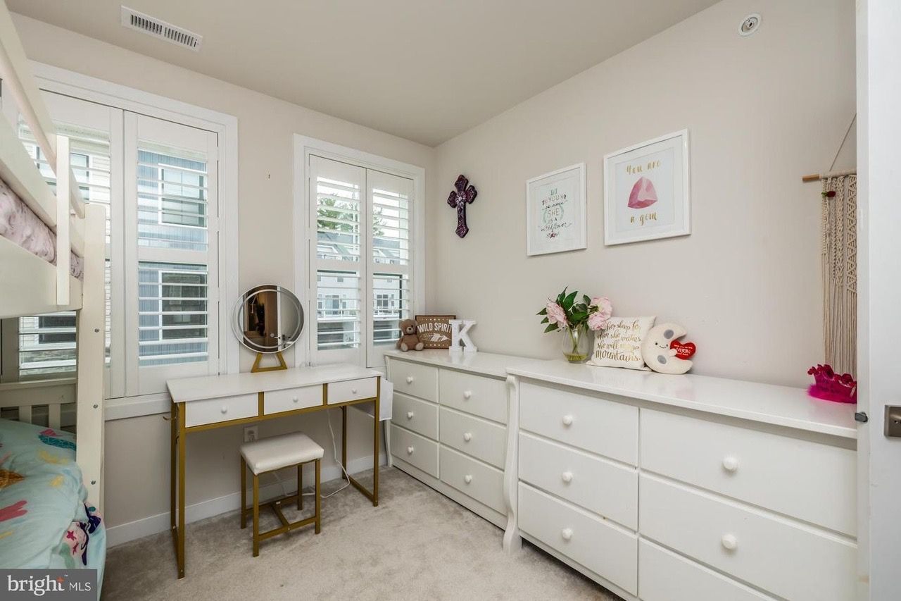 Bedroom with white furniture, shutters, and artwork; a bunk bed is visible on the left.