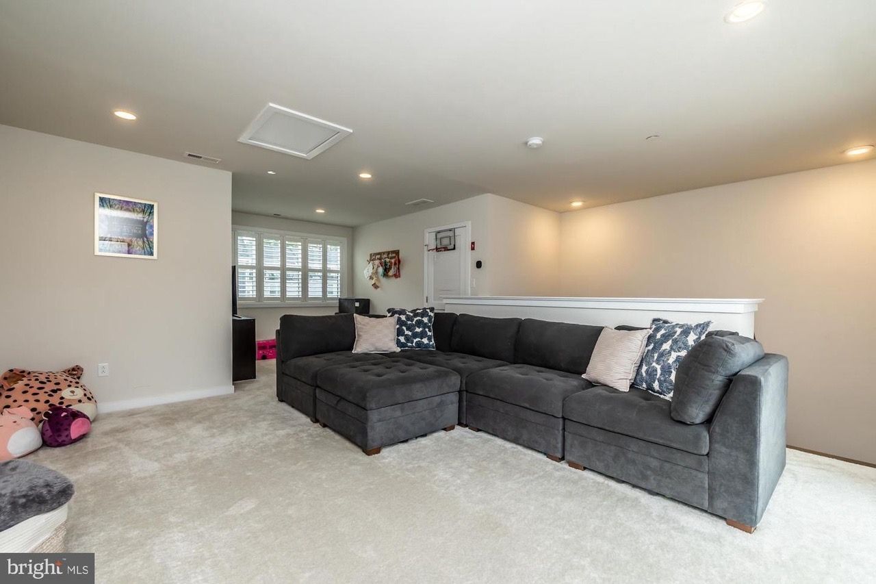 Cozy, gray sectional sofa in a room with light carpet, pillows, and recessed lighting.