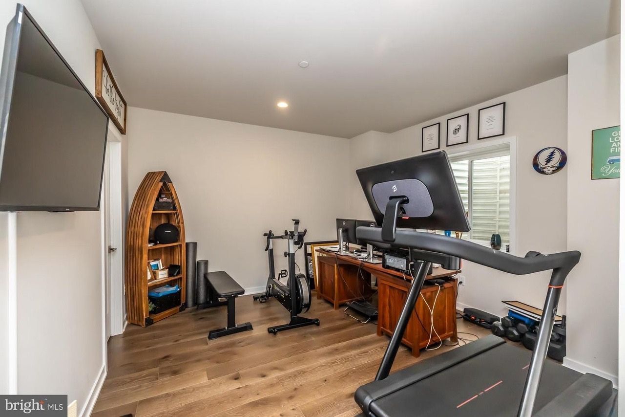 Home gym with treadmill, desk, exercise bike, weights, TV, and wooden boat-shaped shelf.