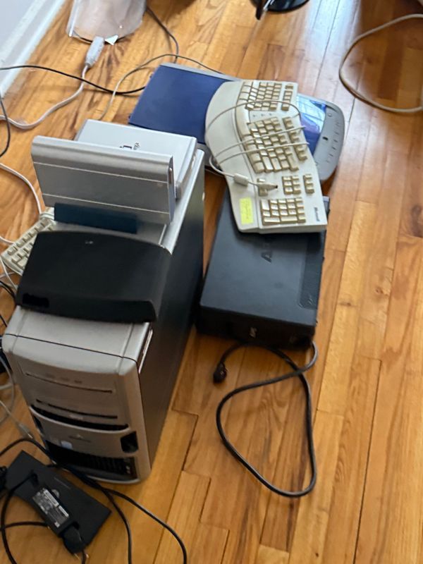 Computers, keyboards, and accessories piled on a hardwood floor.