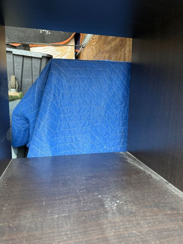 A dark cabinet interior with a blue moving blanket inside.