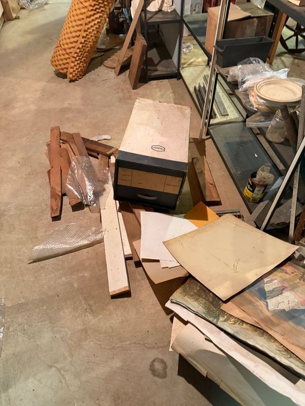 Cluttered basement floor with wood scraps, papers, and a box near a display case and basket.
