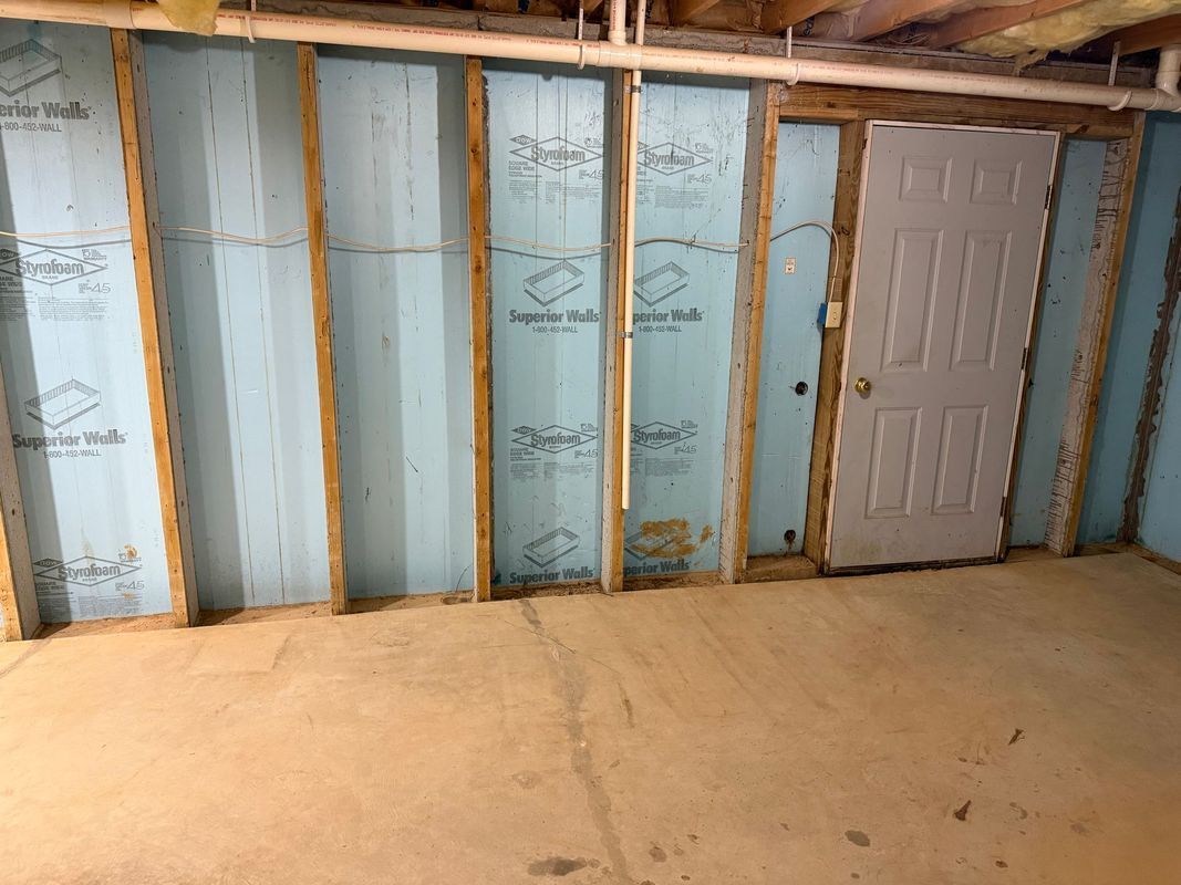 Interior view of a basement room with blue insulation between wood studs and a closed white door.