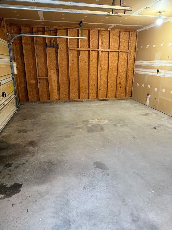 Empty garage with concrete floor, wood-paneled wall, and drywall. Garage door is open.