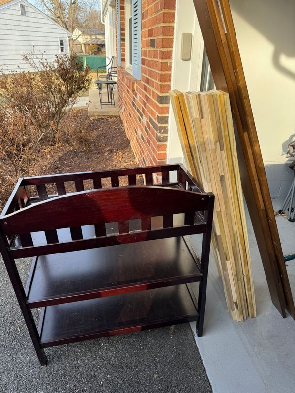 Dark wood changing table with shelves, next to wood pieces leaning against a brick wall.